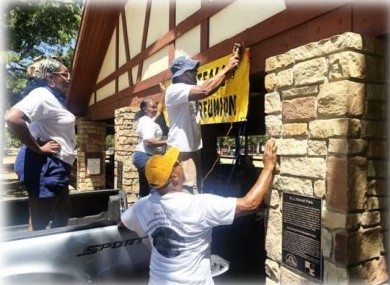Family hanging the Wheatfall Family Reunion banner on the pavilion