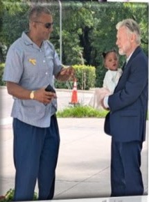 Two men talking outside the church, one holding a baby