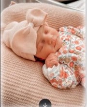 Newborn Mabel sleeping in a floral outfit and pink bow