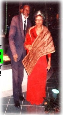 Raymond Sr. in a suit and Annie D. in a red dress and fur wrap, standing together