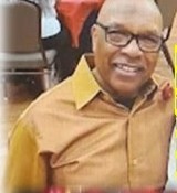 A smiling family elder in a gold shirt and glasses