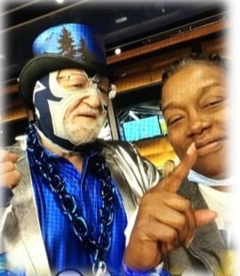 A super fan in a blue luchador mask and top hat posing with a family member