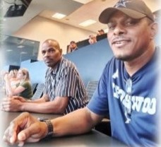 Two men smiling at a table, one in a Cowboys cap